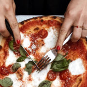 Gros plan sur des mains de femme découpant une pizza.