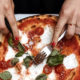 Gros plan sur des mains de femme découpant une pizza.