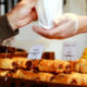 Deux mains au-dessus de pains au chocolat. C’est un boulanger qui remet une viennoiserie à un client.