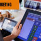 Le mot "marketing" apparaît en haut de l’image sur laquelle on voit un commerçant utiliser son logiciel de caisse pour faire du marketing.