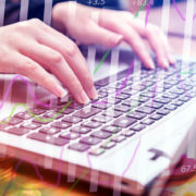 Mains d'une femme tapant sur le clavier d'un ordinateur. Elle gère ses affaires sur cet ordinateur et des petites piles de pièces et des courbes statistiques en hausse montrent qu'elle y gagne de plus en plus d'argent.