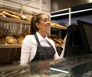 Dans une boulangerie pâtisserie, une jeune serveuse souriante enregistre la commande d’un client sur sa caisse enregistreuse.
