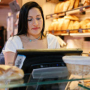 Une commerçante, dans sa boulangerie, semble se demander, devant sa caisse, quel logiciel de caisse PrestaShop choisir pour son commerce.