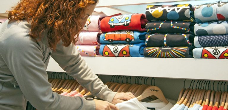 Une vendeuse rousse range les rayons d'un magasin de prêt-à-porter.