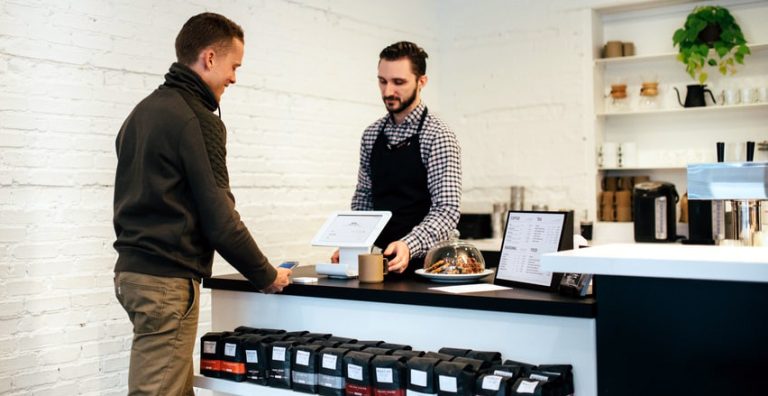 Dans un commerce, vendeur et client souriants, une caisse enregistreuse connectée entre les deux.