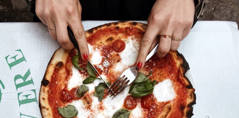 Gros plan sur des mains de femme découpant une pizza.