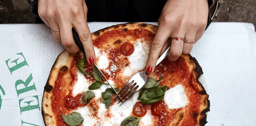 Gros plan sur des mains de femme découpant une pizza.
