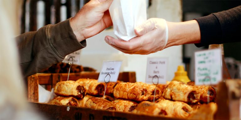 Deux mains au-dessus de pains au chocolat. C’est un boulanger qui remet une viennoiserie à un client.