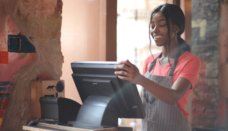 Une jeune commerçante derrière sa caisse, souriante, heureuse d’utiliser un logiciel de caisse simple et efficace.