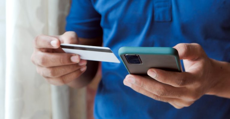 Un client, carte bancaire et iPhone en mains, effectue un achat sur Internet qui sera géré par une caisse enregistreuse en ligne.