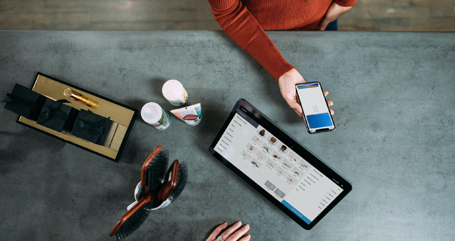 « Logiciel de caisse : quelle utilité ? », semble se demander cette dame au comptoir d’un magasin, portable à la main, face à une commerçante tenant sa caisse enregistreuse installée sur une tablette.