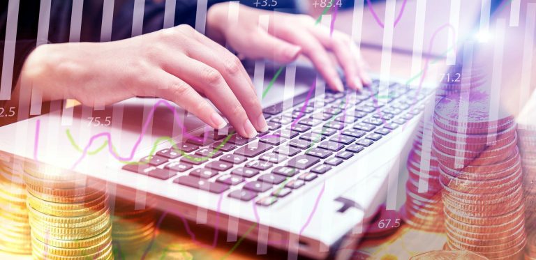 Mains d'une femme tapant sur le clavier d'un ordinateur. Elle gère ses affaires sur cet ordinateur et des petites piles de pièces et des courbes statistiques en hausse montrent qu'elle y gagne de plus en plus d'argent.