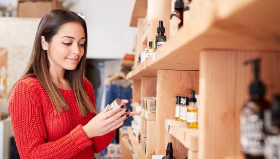 Jeune femme examinant un flacon dans les rayons d'un magasin utilisant un logiciel de caisse magasin produits de beauté.