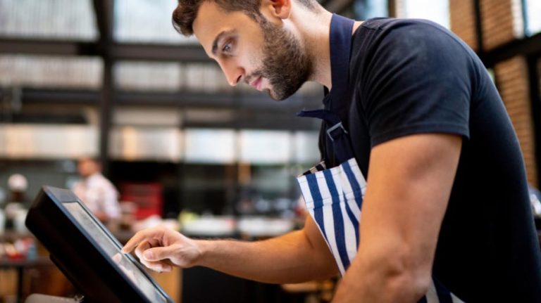 Jeune commerçant dans son magasin, penché sur son écran, utilisant son application caisse enregistreuse.