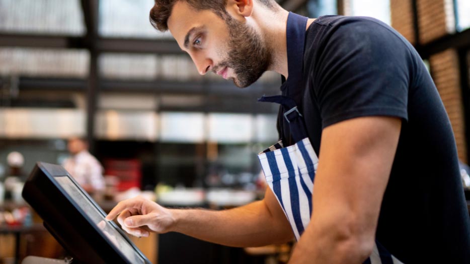 Jeune commerçant dans son magasin, penché sur son écran, utilisant son application caisse enregistreuse.