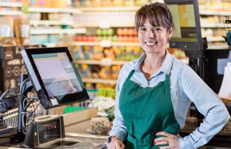 Commerçante souriante à côté de sa caisse enregistreuse tactile.