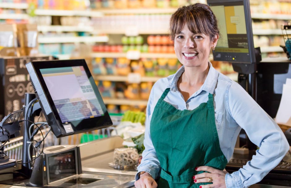 Commerçante souriante à côté de sa caisse enregistreuse tactile.