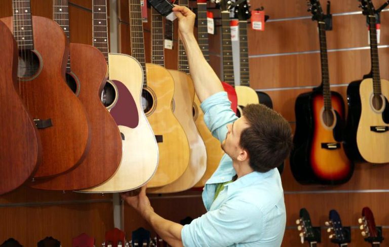 Jeune homme choisissant une guitare dans le rayon d’un magasin utilisant un logiciel de caisse magasin matériel de musique.