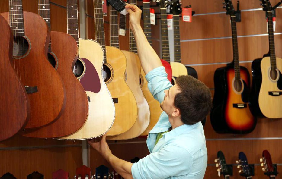 Jeune homme choisissant une guitare dans le rayon d’un magasin utilisant un logiciel de caisse magasin matériel de musique.
