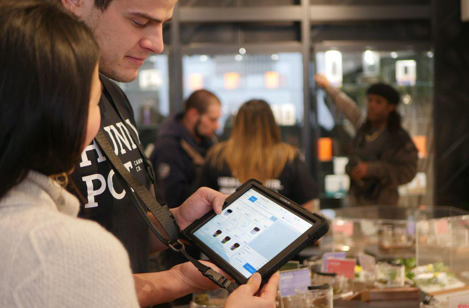 Dans un magasin, client et commerçante tenant dans les mains une tablette transformée en caisse enregistreuse.
