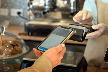 Transaction à la caisse d’un magasin. La main du client tient un Smartphone, celle de la commerçante, un TPE.